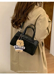Dettaglio borsa Kelly in pelle nera con ciondolo orsetto su modella in trench