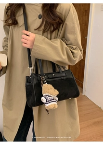 Dettaglio borsa Kelly in pelle e camoscio nera con ciondolo a orsetto su trench beige