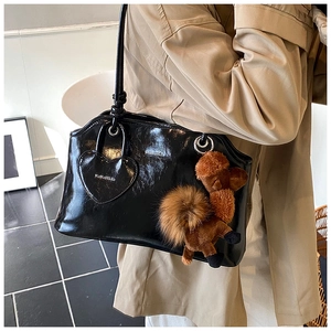 Dettaglio borsa a spalla in pelle verniciata nera con tasca a cuore e ciondolo alpaca