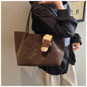 Detail of dark brown suede tote bag with teddy bear pendant worn by a model