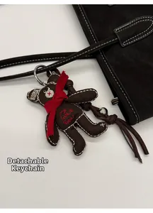 Detail of a brown plush bear charm with red scarf and embroidery on a black bag