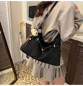 Detail of black matte hobo bag with a cute dog plush charm and adjustable strap
