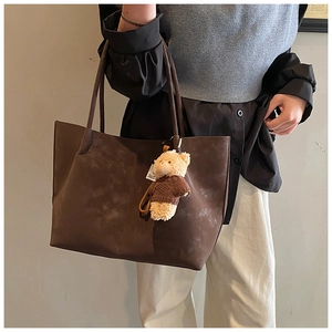 Detailed side view of large brown suede tote bag featuring a cute bear doll pendant