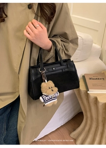 Dettaglio borsa in pelle nera con doppi manici e un simpatico ciondolo a forma di orsetto