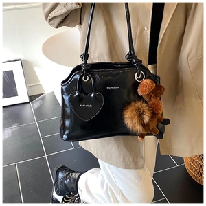 Dettaglio borsa a spalla nera lucida con ciondolo a cuore e accessorio orsetto di peluche