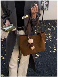 Chic brown suede tote bag with charm pendant held by model in autumn street style