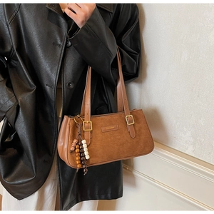 Dettaglio della borsa sottobraccio in pelle scamosciata marrone con ciondolo vintage