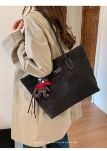 Detail of black suede tote bag featuring white stitching and a cute bear bag charm