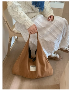 Close-up of brown suede tote bag with SEEYOU label held by model in casual setting