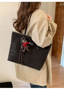 Detail of black leather tote bag with a fashion label and cute teddy bear charm