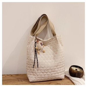 Detail of cream quilted tote bag with lattice stitching and decorative tassel charm