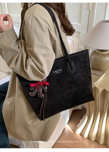 Detail of black suede tote bag with contrast stitching and fashion tag displayed on shoulder