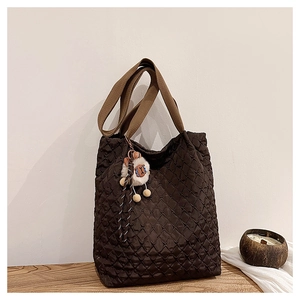 Detail view of dark brown quilted tote bag featuring a cute plush lamb charm on a desk