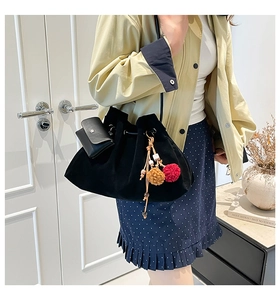 Detail view of black velvet bucket bag with drawstring closure and colorful pompom tassel