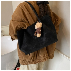 Detail of a black faux suede tote bag featuring a cute teddy bear charm on a slim strap