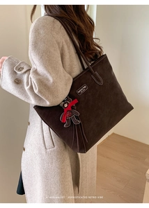 Close-up of deep brown suede tote bag featuring a leather logo patch and cute bear charm