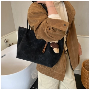 Close-up of black suede tote bag with cute brown bear charm and long leather straps