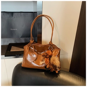 Dettaglio borsa a spalla marrone scuro lucido con ciondolo a cuore e accessorio in peluche
