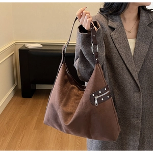 Brown suede tote bag with rivet details shown on model in a modern indoor setting