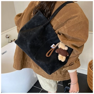 Détail d'un grand sac cabas en daim noir avec un pendentif d'ours en peluche mignon