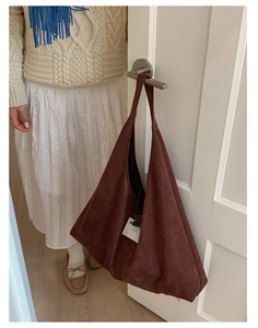Detail of a large dark brown suede tote bag hanging on a door handle in a cozy room
