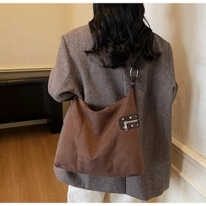 Detail view of brown suede hobo bag with metallic rivets and side zipper on a model