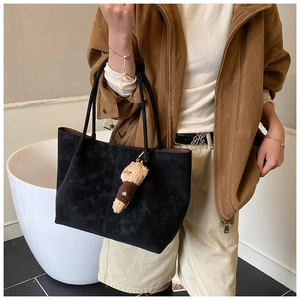 Detail of black suede tote bag with teddy bear pendant and textured surface detail