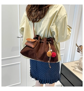 Detail view of brown suede drawstring bucket bag with decorative colorful pompom charm