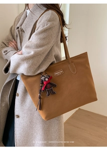 Close-up of brown suede tote bag featuring a teddy bear charm and brand logo detail