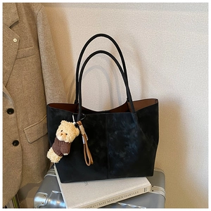 Close-up of black suede tote bag with cute bear charm on metallic luggage