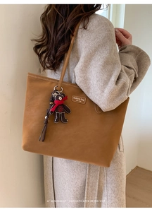 Detail of caramel brown tote bag with fashion logo and black bear charm pendant
