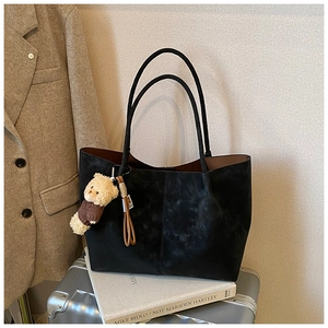 Detailed view of the black suede tote bag with a cute plush bear pendant and long straps