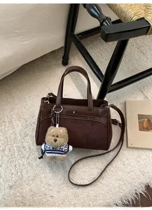 Dettaglio borsa Kelly in camoscio marrone scuro con manici in pelle e ciondolo a orsetto
