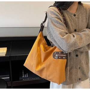 Detail of orange suede shoulder bag showing wide strap with silver metal eyelets