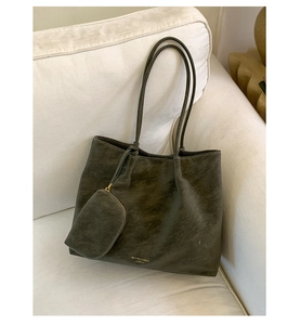 Detail of dark gray matte leather tote bag and mini pouch against a beige sofa
