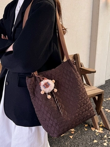 Quilted tote bag in brown with wide strap and plush bear charm shown on a park bench