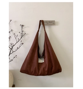 Detail of a large brown suede tote bag with a white SEEYOU label on a minimalist wall