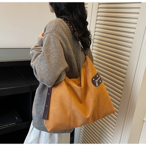 Detail of a large orange tote bag with leather straps and silver studs shown on a model