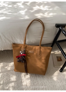 Detail of vintage brown tote bag with leather label and a cute bear charm on a soft rug