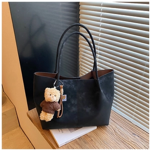 Close-up of black suede tote bag with a cute bear charm on a wooden surface