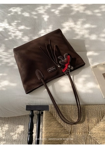 Detailed view of coffee suede tote bag with fringe and cute bear pendant on white fabric
