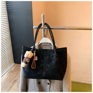 Detail of a large black suede tote bag with a plush bear charm on a wool coat