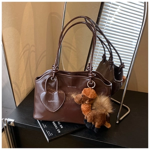 Dettaglio borsa tote in pelle lucida marrone scuro con ciondolo a cuore e accessorio peluche