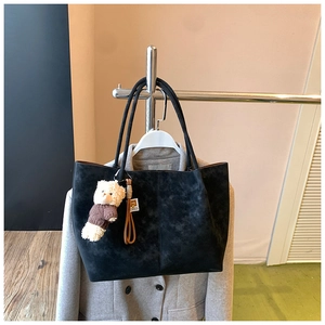 Close-up of large black suede tote bag with a cute plush bear charm on a shoulder strap