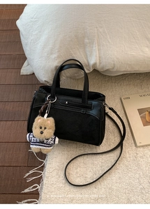 Dettaglio della borsa nera in pelle e scamosciato con ciondolo a orsetto su tappeto bianco