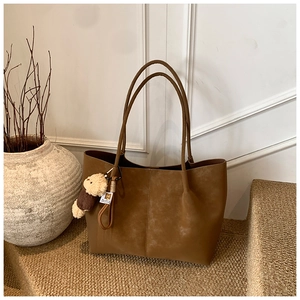 Detail view of a brown suede tote bag with a plush bear charm on a warm textured step
