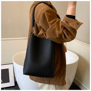 Detail of black pebbled leather bucket bag with wide shoulder strap on brown coat