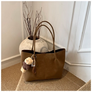 Macro shot of brown suede tote bag with plush bear charm on natural straw mat