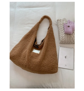 Detailed close-up of brown faux shearling tote bag with SEEYOU label on a soft bed