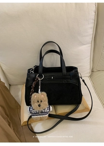 Dettaglio borsa Kelly in pelle nera a grana con fibbia e ciondolo a forma di orsetto blu